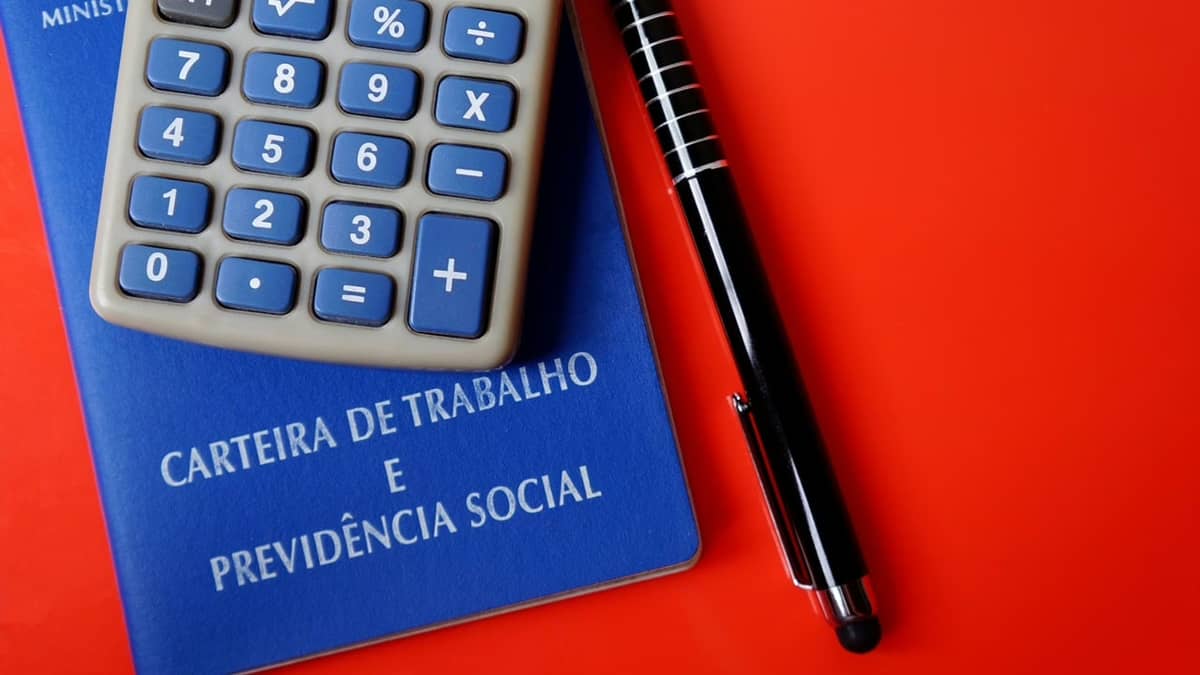 Carteira de trabalho, calculadora e papel escrito "Aposentadoria"