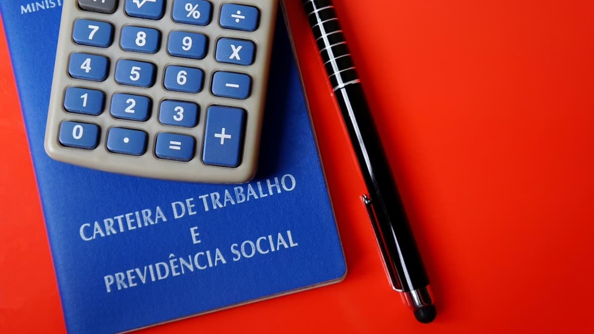 Carteira de trabalho, calculadora e papel escrito "Aposentadoria"